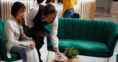 Lobideki müşterilere kahve servisi yapan Asyalı garson, dinlenme odasında bekleyen kadınlar için harika kapıcı servisleri sunuyor. Uçakla seyahat ettikten sonra dinlenmek için içki ısmarlayan turistler..