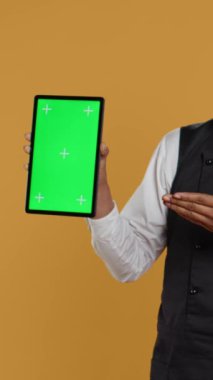 Dikey Video Garson stüdyoda izole edilmiş bir tablet gösteriyor. Hizmet odaklı bir çevrede ve yemek sektöründe çalışıyor. Dost canlısı restoran çalışanları müşterilerine masalarında servis yapıyor.