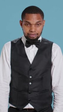 Belboy otel çalışanının dikey video portresi. Kolları bağlı poz veriyor. Smokin ve kravat giymiş özgüven ve profesyonelliği gösteriyor. Kapıcı bellboy konukseverlik sektöründe çalışıyor. Kamera.