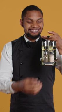 Dikey Görüntü Dost Canlısı Garson, tuz karıştırıcısından tuz döküyor, baharat taşıyor ve beş yıldızlı bir restoranda müşterilere servis yapıyor. Konukseverlikte yemek servisi çalışanı.
