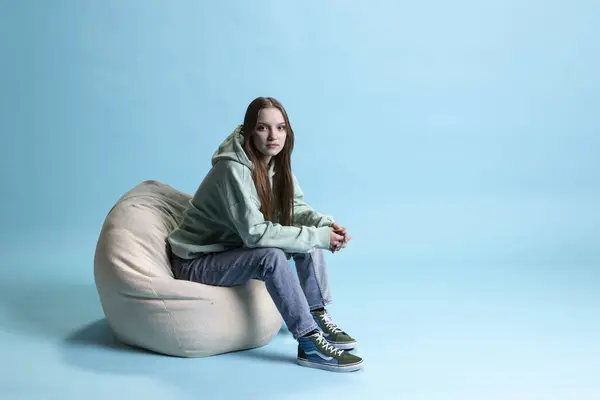 stock image Portrait of woman relaxing on beanbag armchair, isolated over blue studio background. Chilled young person lounged on cozy bean bag, resting at home, having positive mood, studio backdrop