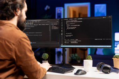 Masaüstü bilgisayarı kullanarak JavaScript programlama dilinde ev geliştirme yazılımı üzerinde çalışan bilişim uzmanı. Sistem mühendisi oturma odasında klavye kullanarak bilgisayarda kod satırları yazıyor.