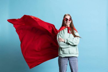 Cadılar Bayramı 'nda süper kahraman kostümü ve maske giyen genç bir kız. Kollarını kavuşturuyor, stüdyo geçmişi var. Çizgi roman kahramanı kılığındaki kadının portresi. Kimliğini gizliyor, gururla duruyor.