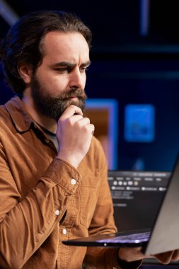 Pensive cybersecurity expert looking confused while using laptop to fix company security vulnerabilities. Contemplative developer feeling worried about potential cyberattacks, close up shot clipart