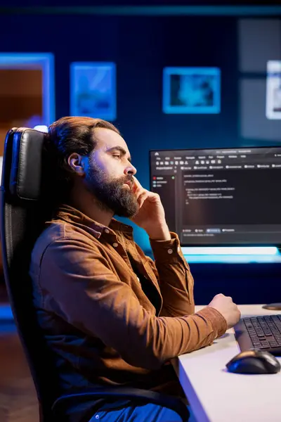 stock image Bored programmer fixing vulnerabilities in software enabling hackers to compromise systems, waiting for shift to end. Impassive man wearied by job, using PC to patch security exposures