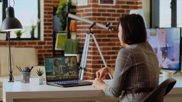 Stock image Remote professional holding q and a session with webinar participants via videoconference meeting in cozy apartment. Online videocall host engaging in online discussions with trainees, camera B