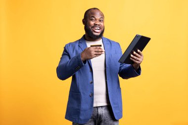 Web sitesine ödeme metodu ekleyen mutlu bir adamın portresi, promosyonlardan ve stüdyo geçmişinden faydalanmaktan memnuniyet duyar. İnternet alışverişi yapmaktan heyecanlanan neşeli insan, tablete kredi kartı verileri yazmak