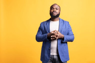 Sarı stüdyo arka planında izole edilmiş, el ele poz veren ve el ele tutuşan Afro-Amerikan bir adam. BIPOC çalışanı endişeli hissediyor, bir şey bekliyor, yana bakıyor.