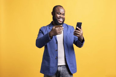 Heyecandan kıvranan neşeli bir adam telefonda ödeme metodu ekleyerek eğleniyor, stüdyo geçmişi var. İnternet alışverişi yaparak, kredi kartı bilgilerini yazarak tatmin eden mest edici kişi