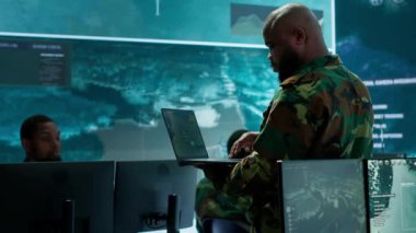 Askeri uzmanlar, ulusal bilginin güvenliği ve bütünlüğünü sağlamak için siber güvenlik, izleme ve veri korumasına odaklanan yüksek teknolojili bir komuta merkezinde çalışıyorlar. Kamera A.