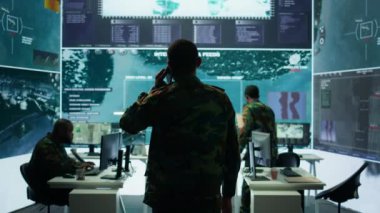 Askeri görevli, potansiyel tehditleri ve gerçek zamanlı verileri takip etmek için gelişmiş teknoloji ve uydu görüntüleriyle çalışan bir görev kontrol merkezinde telefon görüşmelerine cevap veriyor. İstihbarat faaliyetleri. Kamera B.