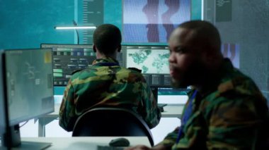 Güvenli bir ofis ortamındaki bir grup asker istihbarat analizi ve stratejik planlama konusunda işbirliği yapıyor. Ulusal güvenlik ve operasyonel verimliliği korumak için önemli çabalar. Kamera A.