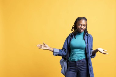 Umursamaz kadın omuz silkme hareketi yapıyor, kayıtsızlık ve ilgisizlik gösteriyor. Umursamaz BIPOC çalışanı umursamaz el hareketi yapıyor, stüdyo arka planında izole edilmiş.