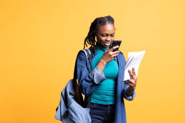 İş arkadaşına göndermek için okul ödevinin fotoğrafını çeken Afrikalı Amerikalı bir kadın. Stüdyo geçmişinden izole edilmiş. Sınav için gerekli bilgilerle birlikte öğrenci fotoğrafları