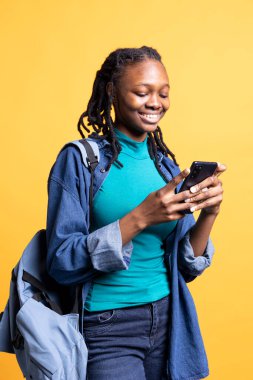 Parlak kız okul arkadaşına cep telefonuyla mesaj atarken, komik mesajlar okurken gülüyor. Cep telefonundan arkadaşlarıyla sohbet eden neşeli genç bir kadın stüdyo arka planında izole edilmiş.