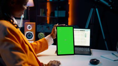 Afrika kökenli Amerikalı kız elinde yeşil ekran düzeniyle tablet tutuyor, finansal ya da ekonomik kurslar için veri analizi yapıyor. Öğrenci cihazda izole edilmiş maket görüntüsü kullanıyor, evden çalışıyor. Kamera B.