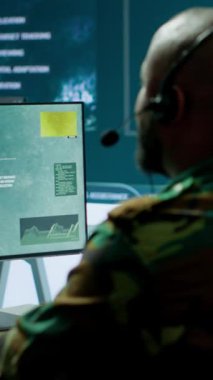 Gelişmiş bilgisayar ve büyük ekran kullanarak, güvenlik önlemlerini arttırmak ve verileri işlemek için uydu sistemlerini izleyen bir operasyon üssünde dikey video askeri personel. Yüksek teknoloji ordu teçhizatı