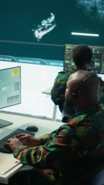 Gelişmiş bilgisayar ve büyük ekran kullanarak, güvenlik önlemlerini arttırmak ve verileri işlemek için uydu sistemlerini izleyen bir operasyon üssünde dikey video askeri personel. Yüksek teknoloji ordu teçhizatı