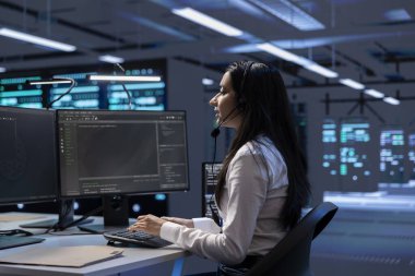 Veri merkezi destek uzmanı ekipman bakımını yapan, mikrofonla konuşan mühendislik ekibini destekliyor. Sunucu çiftliğindeki kadın mikrofon kullanan teknisyenleri koordine ediyor