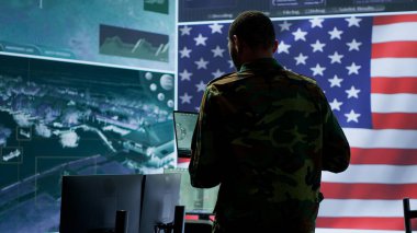 Amerikan askeri üniformalı profesyoneller bilgisayar ve büyük ekran kullanırlar, yüksek teknoloji kontrol merkezinden ulusal güvenliği sağlamak için izleme ve istihbarat üzerinde çalışırlar. Kamera A.