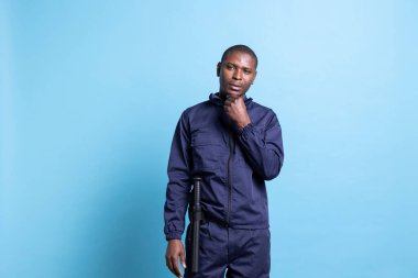 Üniforması ve copu olan düşünceli güvenlik personeli mekanı daha iyi korumanın yollarını düşünüyor, mavi arka plan. Korumak ve korumak için çalışan düşünceli muhafız, devriye servisi..