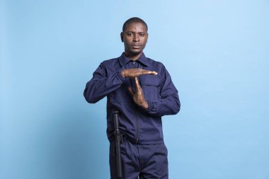 Devriye polisi mavi arka planda bir mola sembolü sunuyor. Koruma görevindeyken ara vermek istiyor. Korumalı üniformalı bir adamın duraksama işareti göstermesi, dinlenmesi gerekiyor..