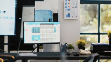 Hesaplama, tahmin ve finansal analiz amacıyla kullanılan boş muhasebe bürosu. Şirket çalışma alanı içinde kimse yok ve bilgisayar monitörlerindeki iş rakamları açık bırakılmış.