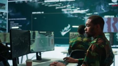 Askeri uzmanlardan oluşan bir ekip, büyük ekran ve dünya haritasını gösteren bir kamera görüntüsü ve radar kullanarak gözetleme faaliyetlerini denetliyor. Operasyonların yüksek teknoloji kontrol merkezi. Kamera B.