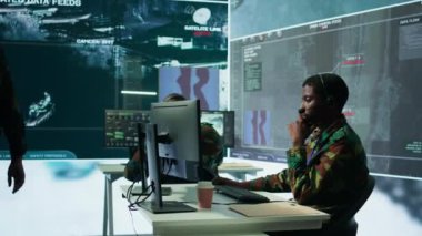 Üniformalı ordu profesyoneli bir görev kontrol merkezinde çalışıyor. Gözetim sistemlerini koordine ediyor ve operasyonlar için istihbarat işliyor. Stratejik planlama ve savunma sağlanıyor. Kamera B.