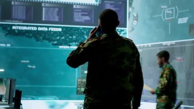 Askeri görevli, potansiyel tehditleri ve gerçek zamanlı verileri takip etmek için gelişmiş teknoloji ve uydu görüntüleriyle çalışan bir görev kontrol merkezinde telefon görüşmelerine cevap veriyor. İstihbarat faaliyetleri. Kamera A.