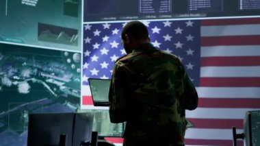 Amerikan askeri üniformalı profesyoneller bilgisayar ve büyük ekran kullanırlar, yüksek teknoloji kontrol merkezinden ulusal güvenliği sağlamak için izleme ve istihbarat üzerinde çalışırlar. Kamera A.