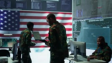 Amerikan askeri üniformalı profesyoneller bilgisayar ve büyük ekran kullanırlar, yüksek teknoloji kontrol merkezinden ulusal güvenliği sağlamak için izleme ve istihbarat üzerinde çalışırlar. Kamera B.