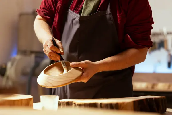 stock image Artisan applying paint on wood object using paintbrush after sanding surface to ensure smoothness, close up. Artist in studio lacquering wooden bowl to build up protective layer