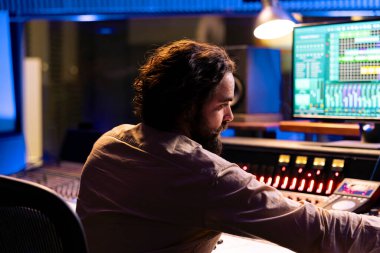 Ses teknisyeni konsolla yeni müzik üretiyor, dijital yazılımla melodileri düzenliyor. Kontrol odasında yetenekli müzik yapımcısı sesleri işliyor, panel paneli kullanıyor.