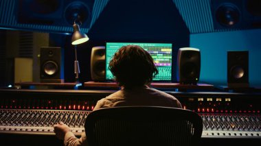 Neşeli müzik yapımcısı, kontrol odasındaki yüksek kaliteli parçanın keyfini çıkarıyor ve projeyi düğmeler ve kaydıraklarla bitiriyor. Ses mühendisi üretimdeki sesleri karıştırıyor. Kamera B.