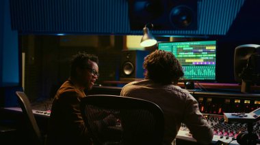 Memnun sanatçı ve iz sürme mühendisi birlikte bir şarkı yarattıktan sonra son sonuçtan mutlu bir şekilde beşlik hareketi yapıyor. Şarkıcı ve yapımcılardan oluşan bir ekip başarılı pist kolajını kutluyor. Kamera B.