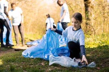Çöp toplayan ve çöp poşetlerinde geri dönüşüm yapan genç kız eylemci, doğal orman ortamını temizleyen ve yasadışı çöplerle mücadele eden. Plastik atık ve çöp toplayan ekolojik gönüllü.