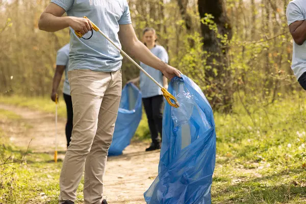 stock image Male volunteer collecting rubbish to fix pollution issues within the habitat, protecting the natural ecosystem. Activist doing voluntary work to clean the woods from trash and plastic waste.