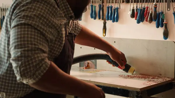 stock image African american woodworker cleaning spindle moulder machine after finishing client commissioned project. Manufacturer using vacuum cleaner on wood shaper, sucking sawdust, camera A