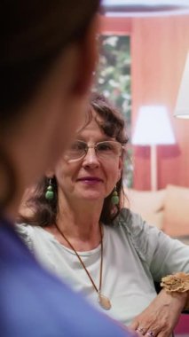 Ev ziyareti sırasında tekerlekli sandalyedeki yaşlı kadına danışmanlık yapan dikey video bakıcısı, iyileşme tedavisi ve sağlık takviyeleri hakkında konuşuyor. Hemşire kıdemli destek ve tavsiye sunar