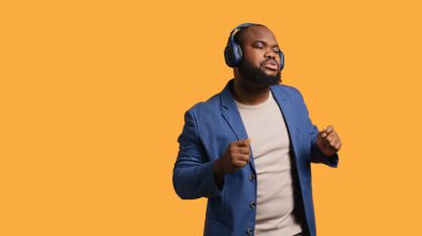 Mutlu Afro-Amerikan insanları eğleniyor, ritim tutarak dans ediyor, kulaklık dinliyor. Neşeli BIPOC adamı kendini eğlendirirken müzik, stüdyo arka planı, kamera B