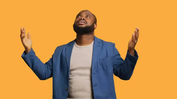 stock image Cheerful pious african american man looking up to sky, waiting for sign from his god. Happy spiritual man doing worship hand gesturing, hoping for miracle, isolated over studio background, camera A