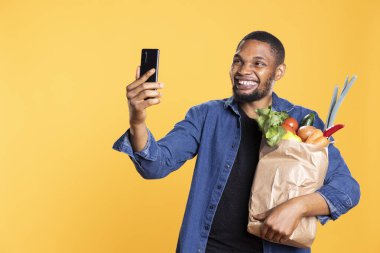 Afro-amerikan yetişkinler alışveriş yaparken gülümserken alışverişte başarılı oluyorlar. Neşeli pozitif insan akıllı telefon uygulamasından selfie çekiyor..
