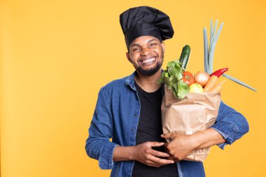Afro-Amerikalı aşçı, vejetaryen yemeği hazırlamak için biyolojik ürünlerle dolu bir poşet taşıyor ve etik kaynaklı malzemelerle yemek pişirme konusunda heyecanlı. Sürdürülebilir yaşam tarzı.