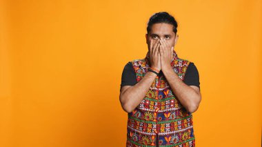 Anxious indian man covering face with palms, worried about future, isolated over studio background. Tense person massaging temples, bothered by troubling news, feeling distressed, camera B clipart