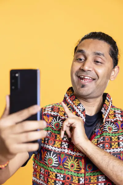 stock image Joyous indian narcissistic man using cellphone to take selfies from all angles. Vain social media user taking photos using phone selfie camera, smiling happily, studio background