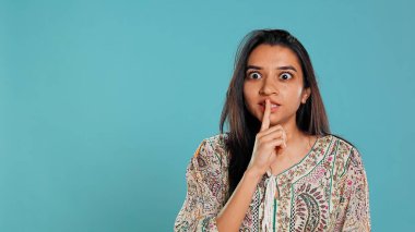 Annoyed indian woman doing shushing hand gesturing, irritated by noise, having negative mood. Person placing finger on lips, doing quiet sign gesture, isolated over studio background, camera B clipart