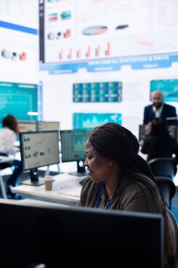 Proje lideri şirket genel merkezinde büyük ekranlı bir pazar araştırması yaparak girişimin ilerlemesini sağlıyor. Mevcut organizasyonel durumu araştıran finans müdürü.