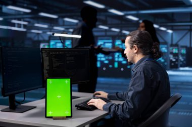 Programcı, veri merkezi depolama ekipmanında yeşil ekran tableti üzerinde çalışıyor. Bilgi İşlem uzmanı, sunucu çiftliğinde ağ bileşenlerini kullanarak çok büyük miktarda bilgisayar sağlıyor.
