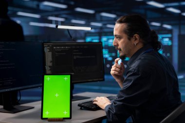 Veri merkezinde olası bir arıza var mı diye kontrol etmek için izole ekran tableti kullanan teknisyen. Bilgi İşlem uzmanı sunucu çiftliğindeki hasarları önlemek ve kritik sistemleri izlemek için modelleme cihazı üzerinde çalışıyor